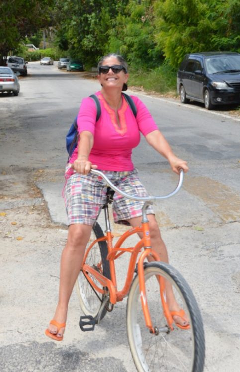 A smiling woman in pink shirt leans back on an orange cruiser bicycle