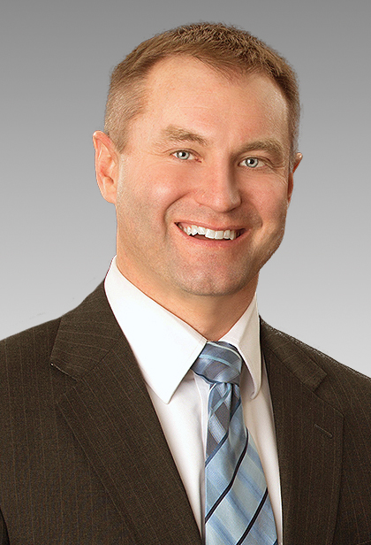 A smiling man with blue eyes, blue tie, white shirt, and gray suit jacket