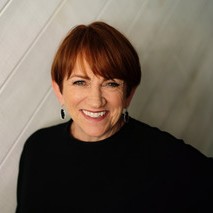 A smiling woman with red lipstick and short, red hair wearing black